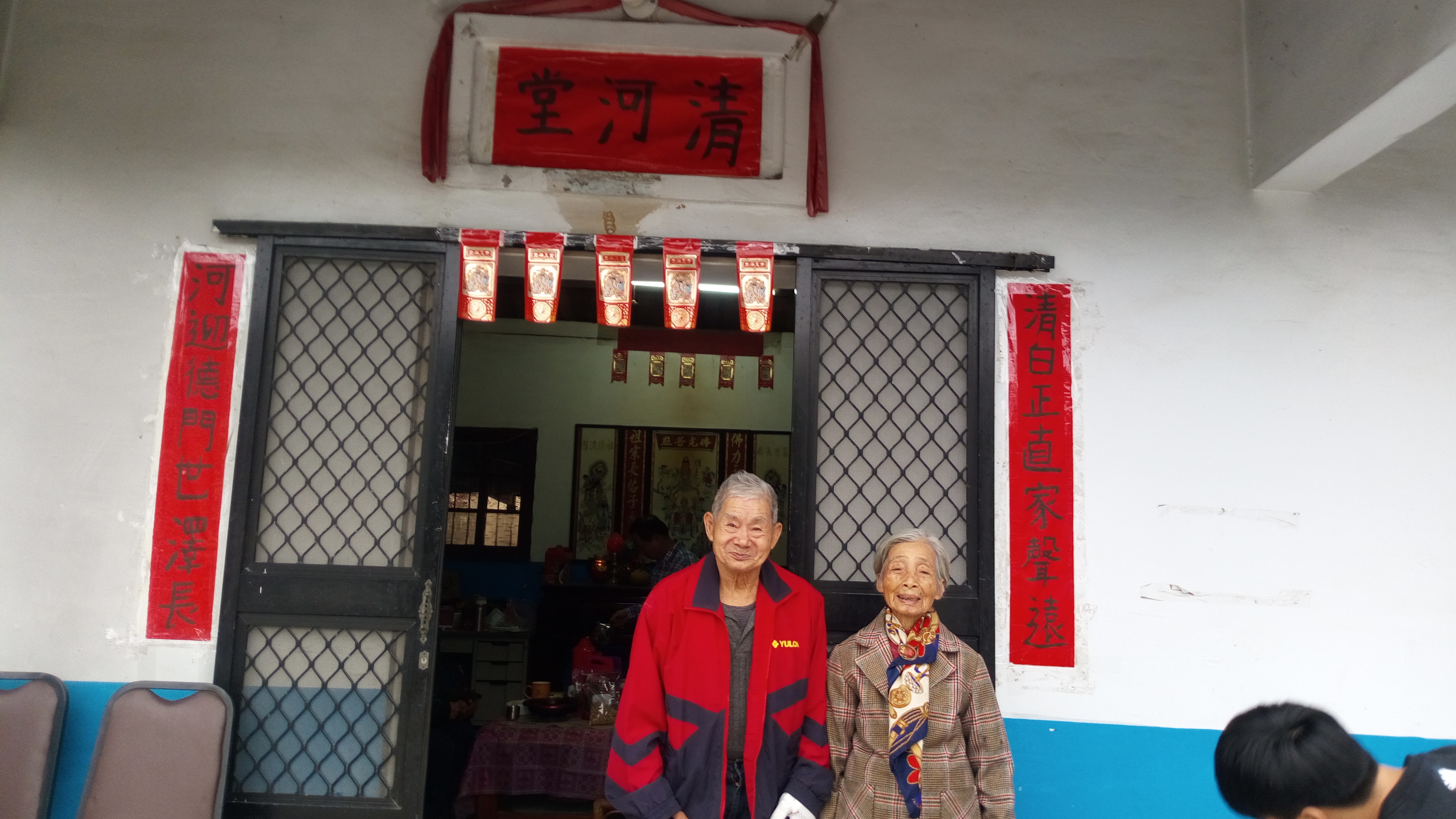 張四妹喜書畫自娛，過年家裡的堂聯也親寫、親貼，字體樸實可愛，圖為4年前她與夫婿張金火在堂聯前合影。何來美攝