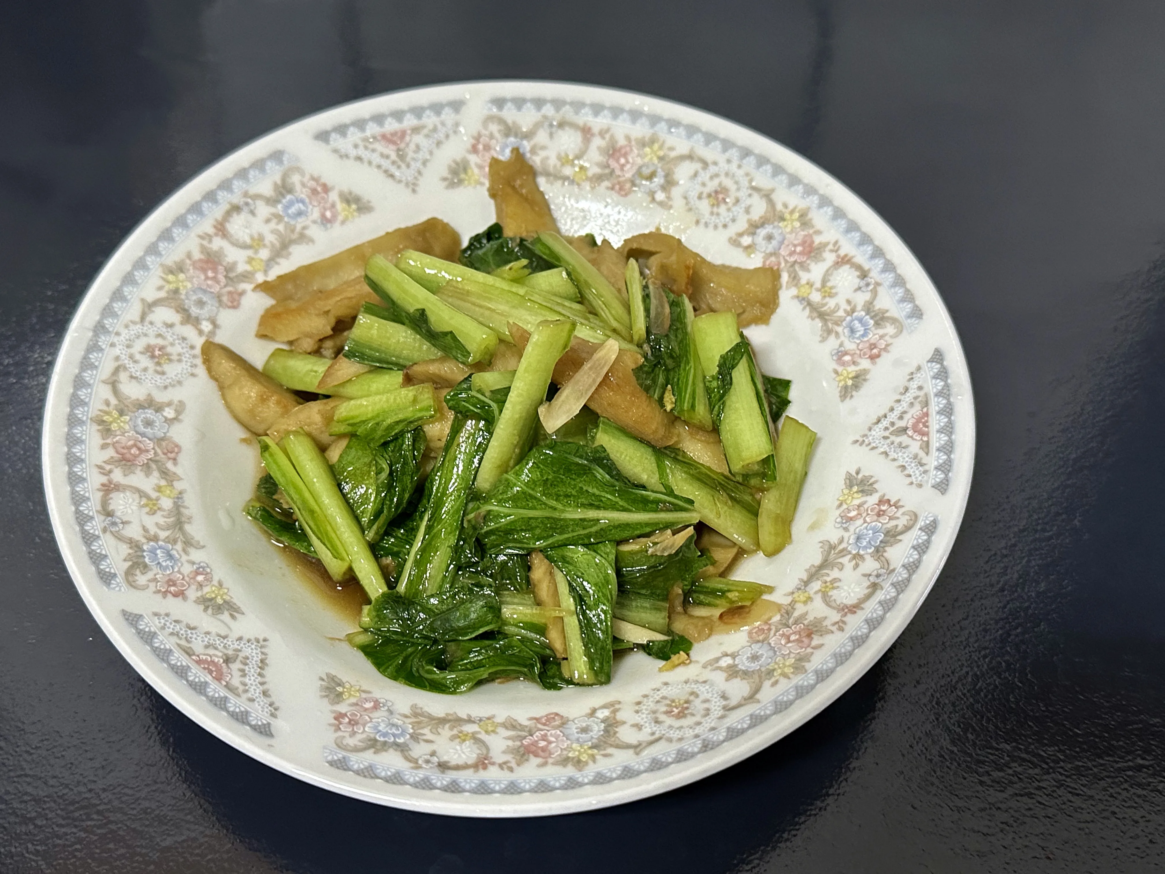 新品種的蕒仔（劍葉萵苣）炒麵筋，以蒜片與麻油提味；作法，麵筋用豬油煎赤，下蒜片炒香，再把蕒仔下鍋，起鍋前以麻油沿鍋邊繞一圈，盛盤。作者提供