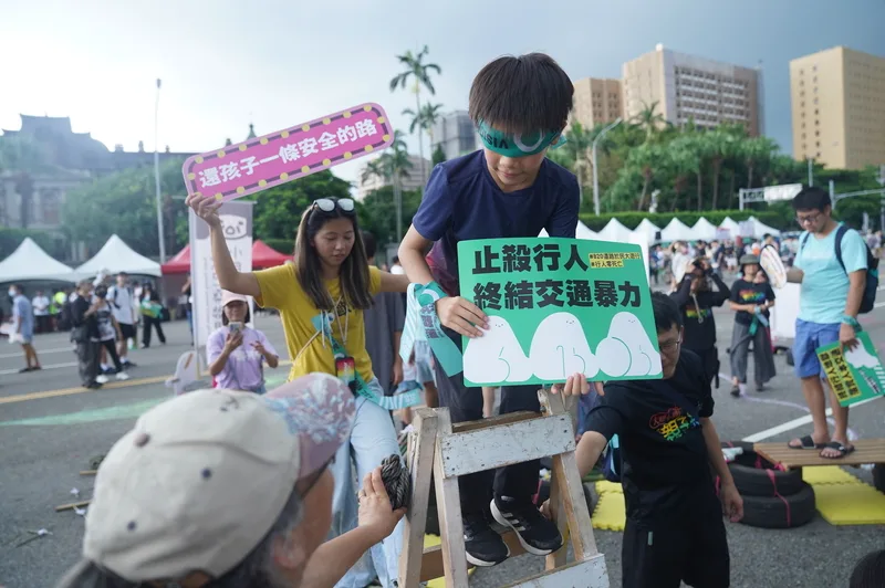 關心行人路權議題的民眾參與遊行活動，還有小朋友拿著活動標語體驗交通安全相關遊戲。中央社