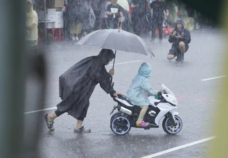 活動現場有家長在雨中引導孩子體驗騎乘玩具車。中央社