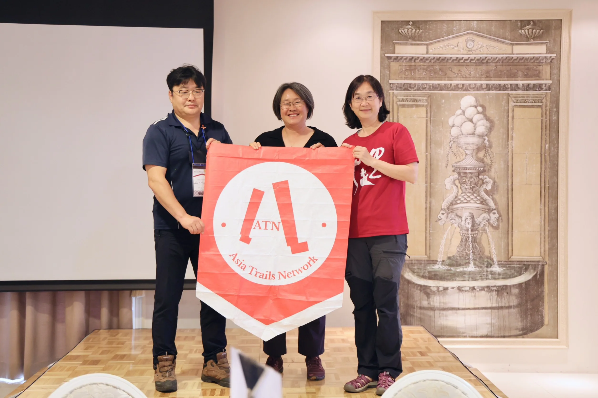 今年6月2日，亞洲步道聯盟年會在鳥取舉行，聯盟將會旗交接予台灣千里步道協會，左起為韓國智異山代表、安殷周、周聖心。台灣千里步道協會提供