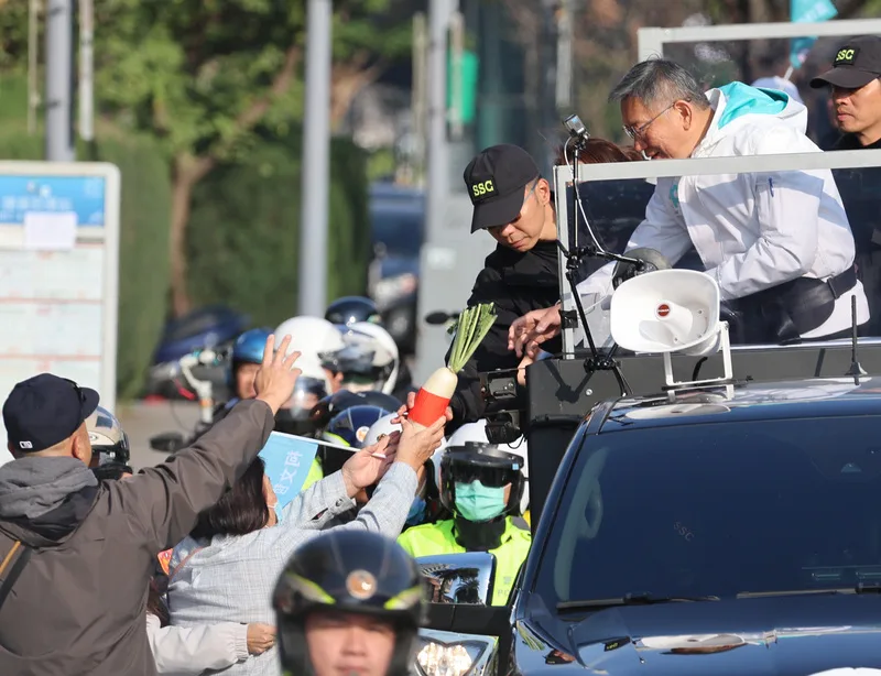 大選投票在即,台灣民眾黨總統候選人柯文哲(前右)11日下午在台北以車隊掃街尋求民眾支持,有熱情民眾送上菜頭象徵「好彩頭」。中央社