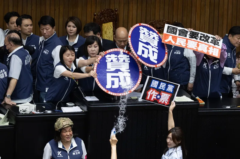立法院長韓國瑜(後中低頭者)發言時被民進黨立委潑水,一旁國民黨立委們趕緊以手牌遮擋。中央社
