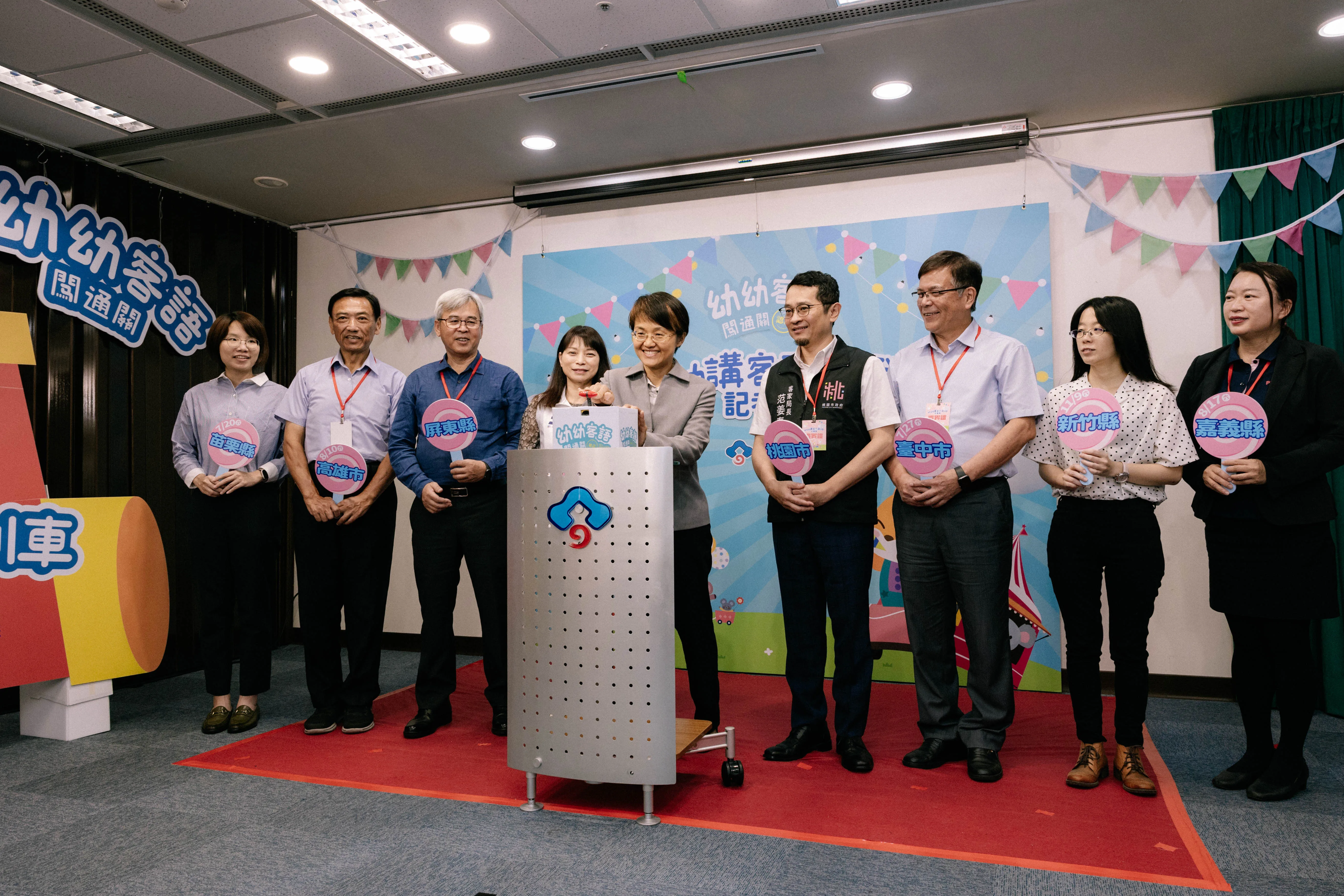 客委會主委古秀妃（中）為今年的幼幼客語闖關認證「幼幼講客列車」按下啟動鈕，新北市客家事務局長林素琴（左四）、桃市客家事務局長范姜泰基（右四）、中市客家事務委員會副主委魏瑞伸（右三）、高市客家事務委員會主秘鍾炳光（左二）、屏縣客家事務處處長李明宗（左三）也一起替活動宣傳。圖/客委會提供