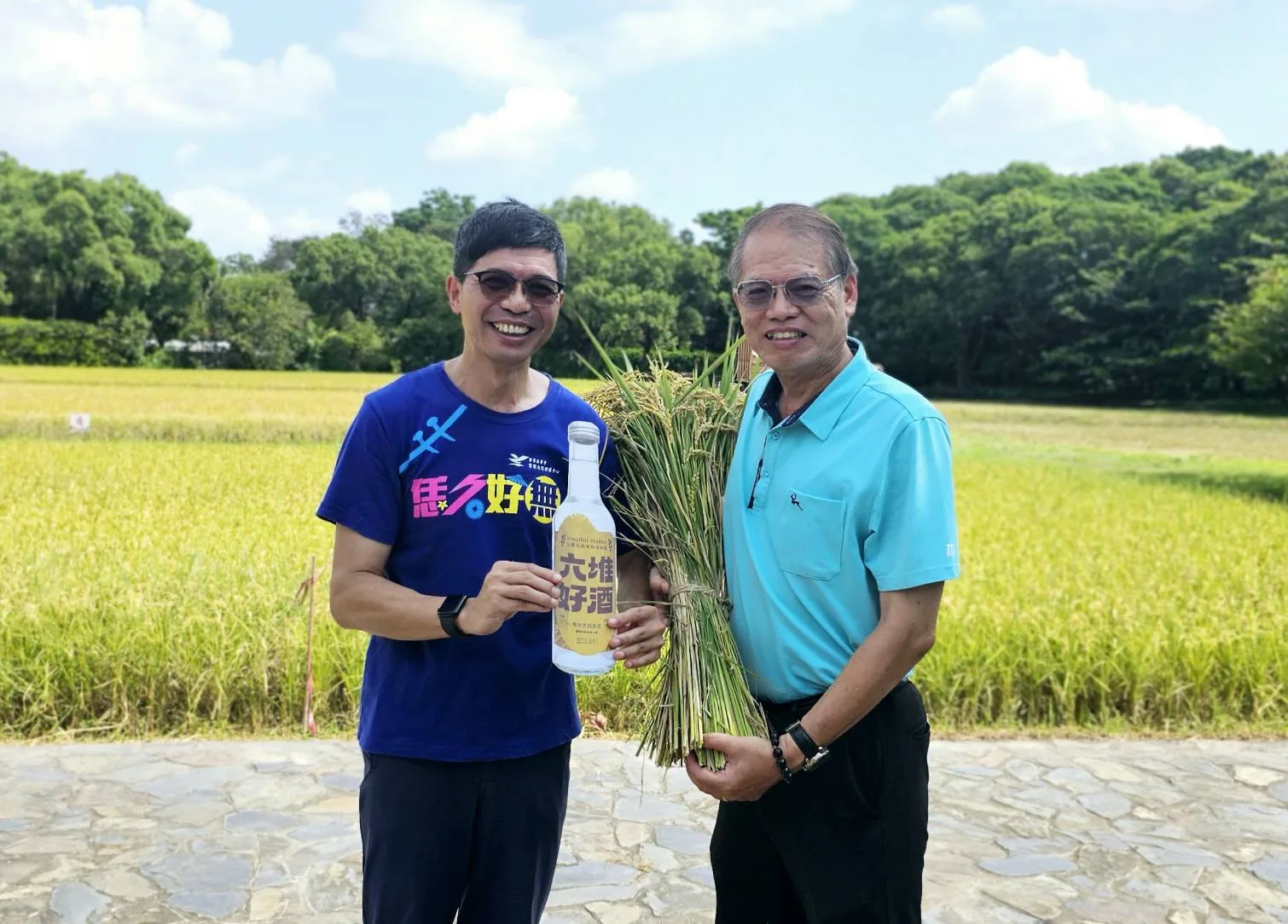 客家委員會客家文化發展中心主任何金樑將部分收成稻米交給屏東酒廠田益民廠長共同開場,延續去年互益合作模式,將部分收成的稻米交由內埔百年酒調配,聯名產出獨特風味的客家料理米酒。照片由六堆客家文化園區提供。
