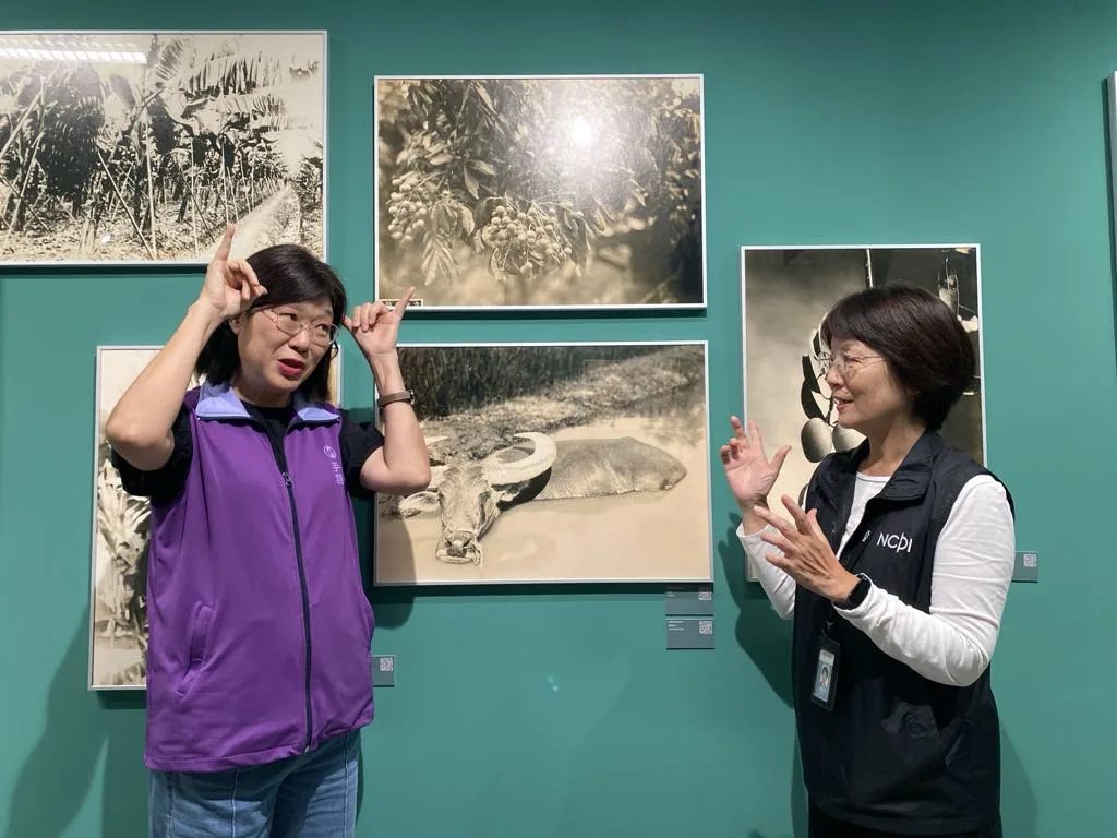 TASLI台灣手語翻譯協會魏如君老師(左)與攝影中心導覽志工鄭玲玲小姐(右)帶領聽語障朋友們認識當期展覽。國家攝影文化中心提供