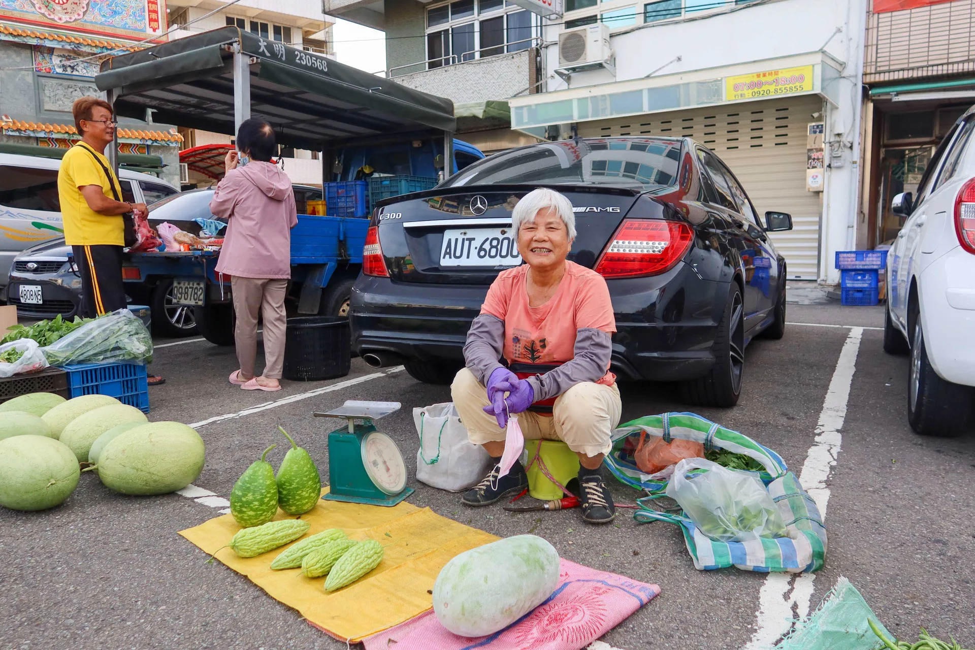 84歲黃月秋自種自賣蔬果已20年，她攤位後方碰巧有輛黑色賓士轎車，顧客笑她是「賓士菜販」，她大笑回敬，自得其樂。何來美攝