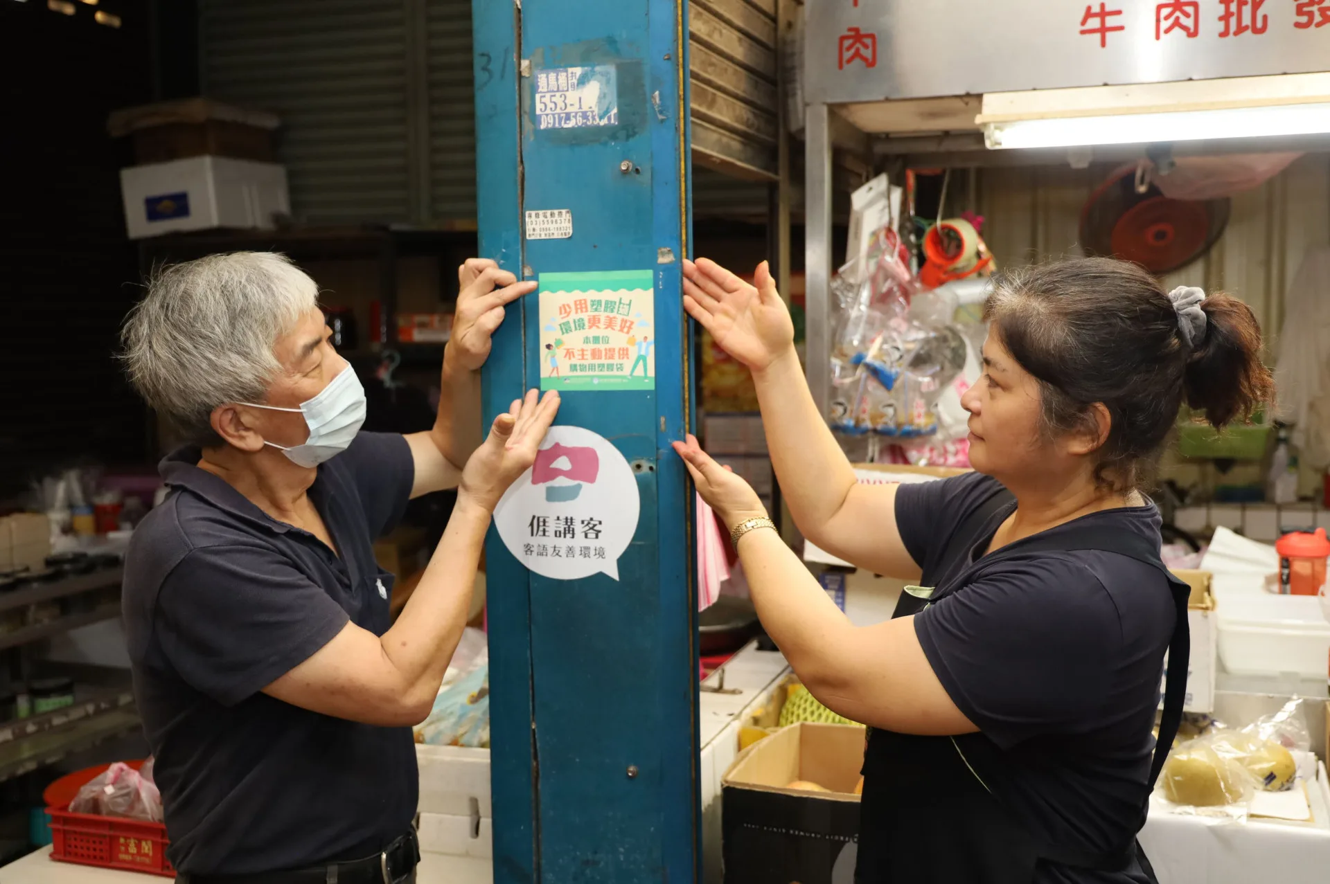 市場人員與攤商貼上宣導使用循環購物袋標語。