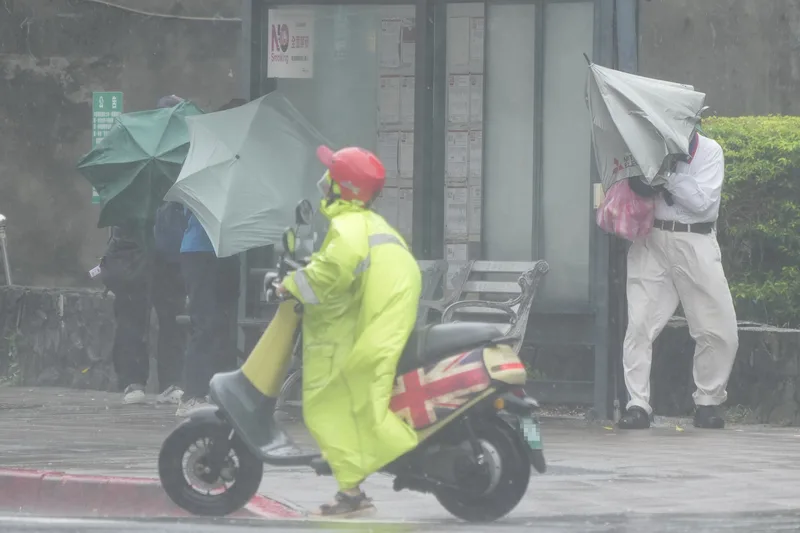 氣象署持續發布豪雨特報,東北季風及颱風風神外圍環流影響,20日台北市及新北市有局部豪雨或大豪雨。圖為民眾在台北市北投區遭強風吹拂,靠在公車站旁躲避。中央社