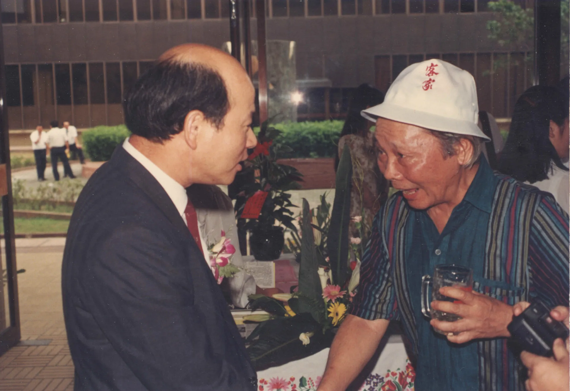竹東陳天鵬醫師等人創辦新竹風雜誌創刊酒會,許信良(左)與鍾肇政(右)相見歡,鍾肇政戴的帽子第二屆客家夏令營學員們每人都有一頂。1991,新竹市,楊國鑫攝