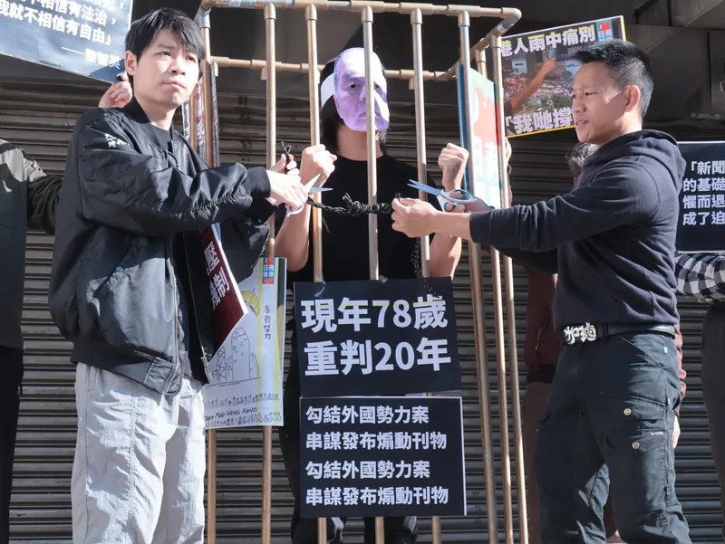 民團、在台港人、台灣新聞記者協會、無國界記者組織、台灣青年世代共好協會、經民連智庫等團體與個人10日上午在立法院群賢樓前聲援香港壹傳媒創辦人黎智英被控違反香港國安法、遭判20年一案,香港邊城青年秘書長馮詔天(左)、在台港人湯偉雄(右)現場演出行動劇。中央社