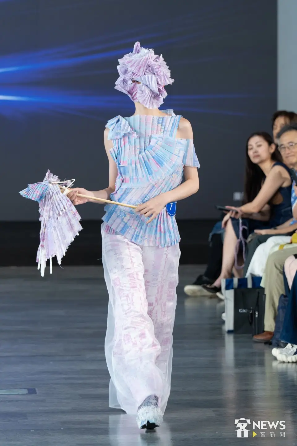 第7號服裝作品以不規則形的淺藍白點綴粉色登場，手持特別飾品並以粉紫面具走秀，僅露出單隻眼睛，造型獨特。李台源攝