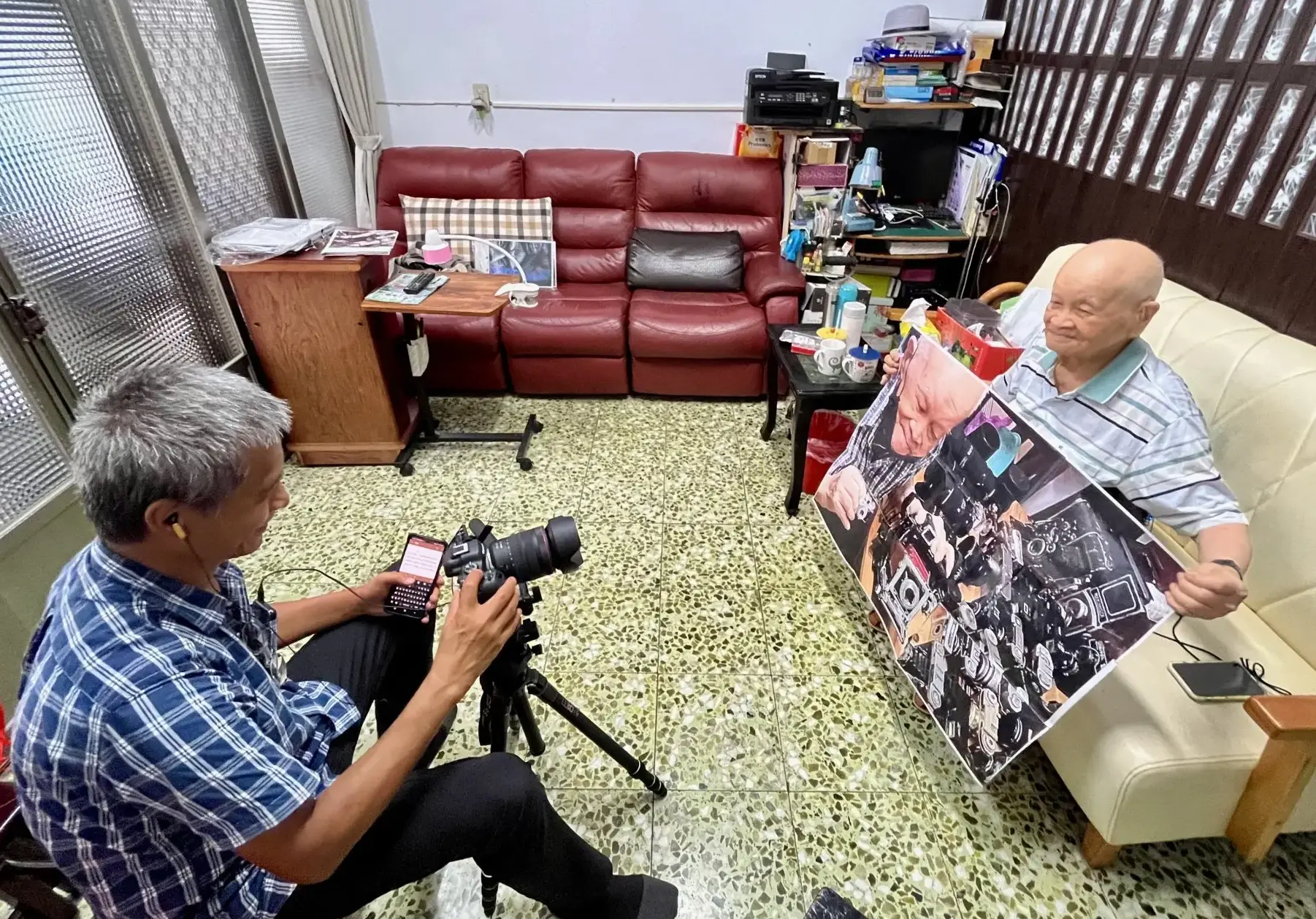資深攝影師黃子明學長為「戰爭世代」計畫拍攝李增昌老先生,老先生攤開修理相機的照片入鏡。徐彩雲攝